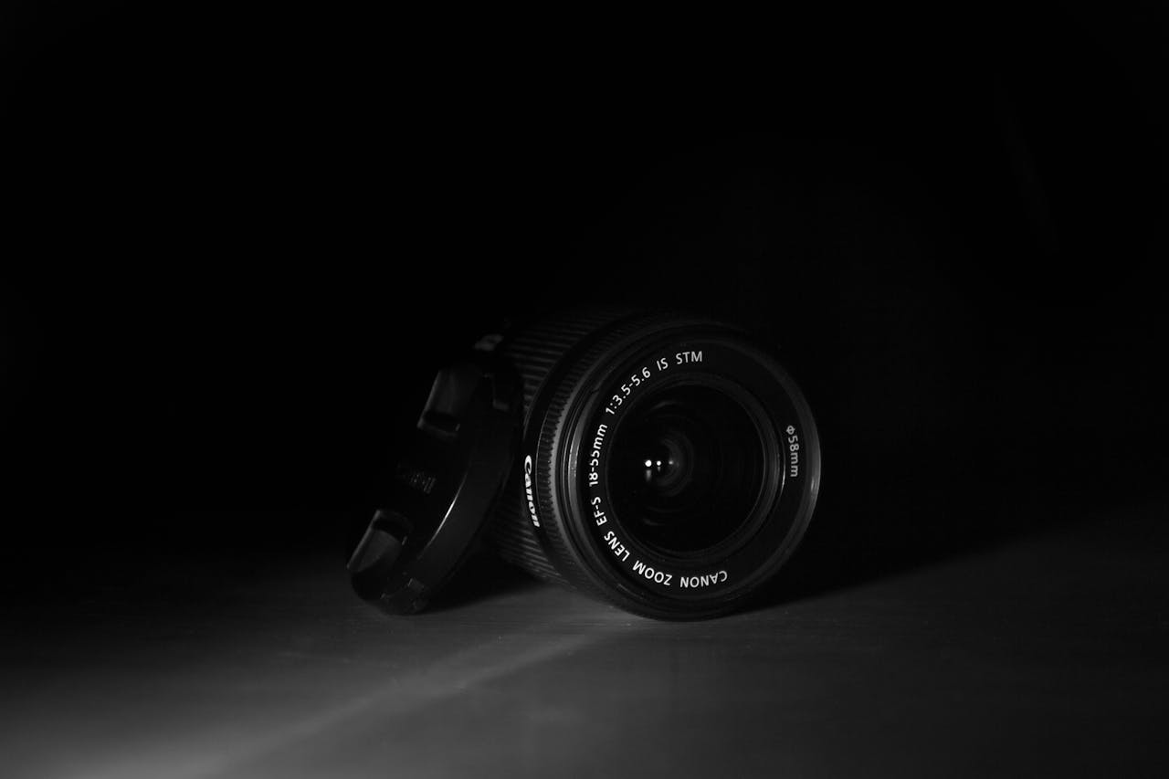 Black and white photo of a DSLR camera lens with cap, showcasing its details in a dramatic, moody setting.