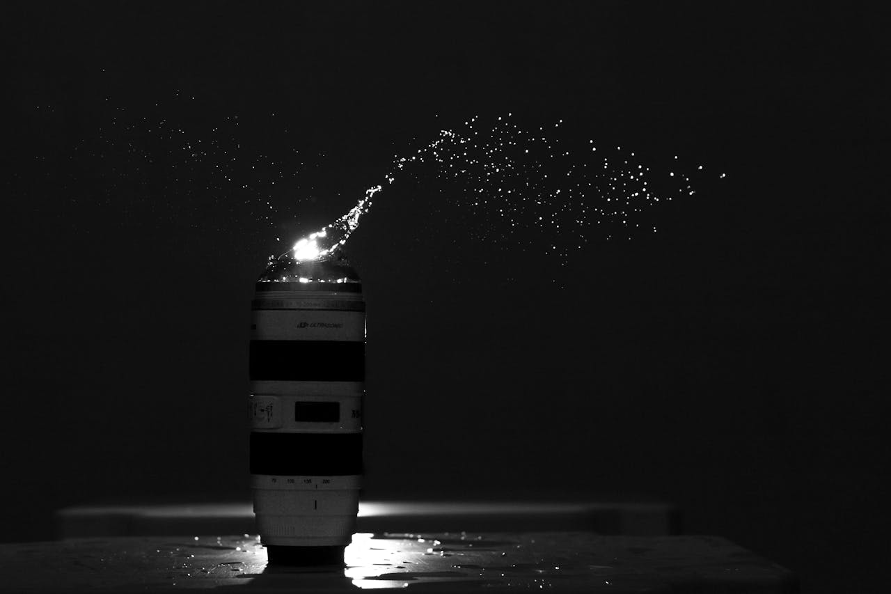 Dramatic capture of water droplets splashing over a camera lens in a dark setting.